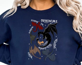 May include: A navy blue sweatshirt with a graphic of five dragons with different colored tails and the text "Dragontails" above them. Each dragon tail has a name: "Scorpion Tail", "Flaregtail", "Morningstartail", "Embertail", and "Daggertail".