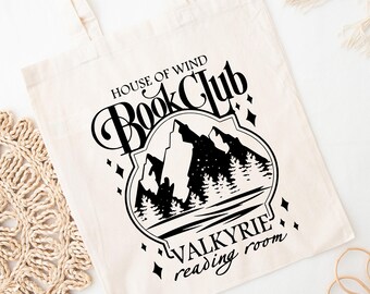 May include: Cream-colored tote bag with black text and graphic. The text reads "HOUSE OF WIND Book Club VALKYRIE reading room" with a mountain and forest design. The bag has two handles and is made of a canvas-like material.