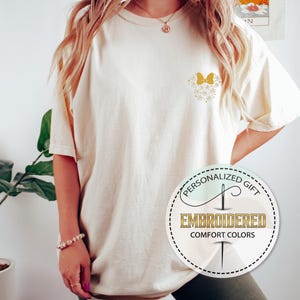 Pu&ograve; includere: Una maglietta color crema con un designo di farfalla ricamata in oro sul petto sinistro. La maglietta &egrave; oversize e ha una vestibilit&agrave; rilassata. Il testo "Regalo personalizzato" e "Ricamato Comfort Colors" &egrave; su un'etichetta circolare.