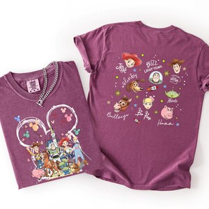 K&ouml;nnte beinhalten: Zwei weinrote T-Shirts mit Toy Story-Charakteren von Disney. Ein Shirt zeigt eine gro&szlig;e Grafik der Charaktere in einer Mickey-Mouse-Kopfkontur. Das andere Shirt hat Charakterportr&auml;ts und Namen. Eine silberne Halskette befindet sich auf einem Shirt.
