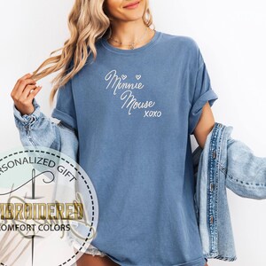May include: A blue t-shirt with the words "Minnie Mouse xoxo" embroidered in white script. The shirt has rolled-up sleeves and is part of a personalized gift collection.