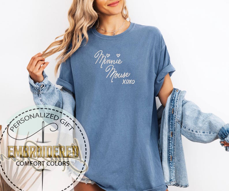 May include: A blue t-shirt with the words "Minnie Mouse xoxo" embroidered in white script. The shirt has rolled-up sleeves and is part of a personalized gift collection.