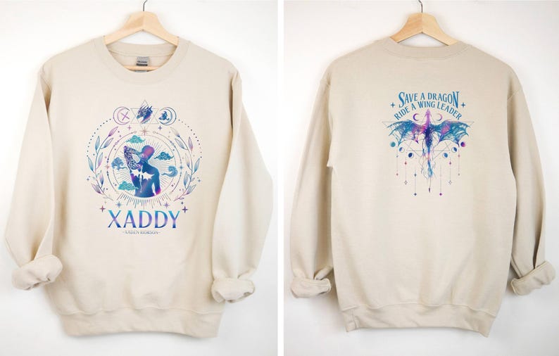 May include: A beige sweatshirt with a graphic print of a person with a dragon on the front and the text "XADDY" below. The back of the sweatshirt has a graphic print of a dragon with the text "Save a Dragon, Ride a Wing Leader".