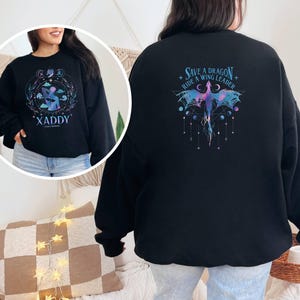 May include: Black sweatshirt with a purple and blue dragon graphic on the back. The text "Save a Dragon Ride a Wing Leader" is printed above the dragon. The front of the sweatshirt has a graphic of a person with the text "XADDY" printed below.
