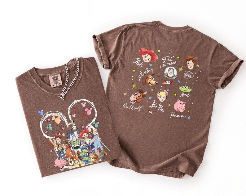K&ouml;nnte beinhalten: Zwei braune T-Shirts mit Toy Story-Charakteren von Disney. Ein Shirt zeigt eine Grafik von Charakteren vor einem Schloss, das andere hat Gesichter und Namen von Charakteren. Eine silberne Halskette befindet sich auf dem ersten Shirt.