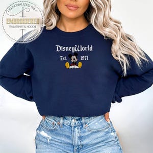May include: Navy blue sweatshirt featuring the embroidered text "DisneyWorld Est. 1971" and a Mickey Mouse graphic. The sweatshirt is a crew neck style and is a personalized gift.