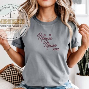 May include: Gray t-shirt with the embroidered text "Minnie Mouse xoxo" in a cursive font. The shirt also features a circular logo with the words "Personalized Gift" and "Embroidered Comfort Colors".