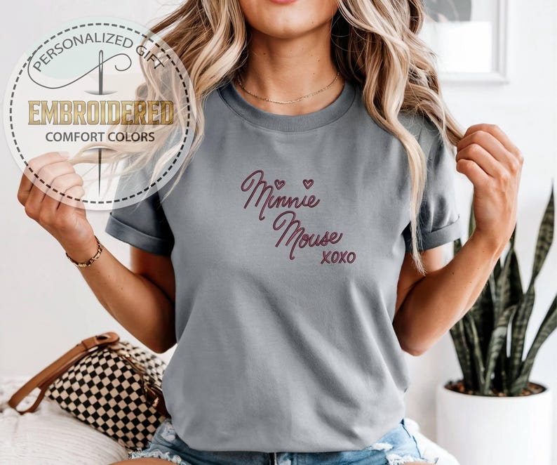 May include: Gray t-shirt with the embroidered text "Minnie Mouse xoxo" in a cursive font. The shirt also features a circular logo with the words "Personalized Gift" and "Embroidered Comfort Colors".
