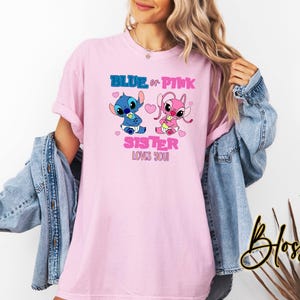 Puede incluir: Camiseta rosa con un gr&aacute;fico de personaje Stitch azul y rosa. El texto "Blue or Pink Sister Loves You" est&aacute; impreso en la camiseta.