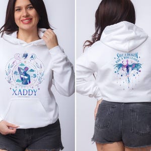 May include: White hoodie with a blue and purple graphic of a person riding a dragon. The text "Save a Dragon, Ride a Wing Leader" is printed on the back of the hoodie. The front of the hoodie has a blue and purple graphic of a person with the text "XADDY" printed below.