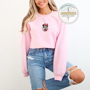 May include: A pink sweatshirt with a cartoon image of Minnie Mouse embroidered on the front. The sweatshirt has long sleeves and a crew neck.