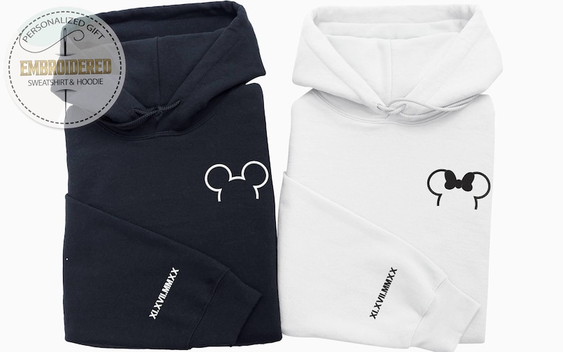 以下が含まれることがあります： 紺色と白の2つのフード付きスウェットシャツ。紺色のスウェットシャツには白いミッキーマウスの耳のデザインがあり、白いスウェットシャツにはミニーマウスのリボンのデザインがあります。どちらも袖に「XL.XVII.MMXX」の文字が入っています。画像には「PERSONALIZED GIFT EMBROIDERED SWEATSHIRT & HOODIE」の文字も含まれています。
