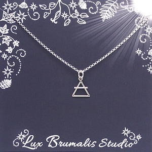 May include: A silver necklace with a simple triangle pendant featuring a horizontal line across the center. The necklace is displayed on a dark blue card with a white floral design and the text "Lux Brumalis Studio".