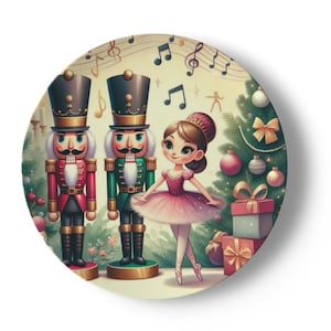 May include: A round ceramic plate featuring a festive Christmas scene. Two nutcracker soldiers stand on either side of a ballerina wearing a pink tutu. A decorated Christmas tree is in the background with presents underneath.