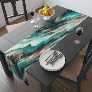 May include: A teal, white, and gold abstract marble table runner with a modern design. The runner is laid on a dark wood table with a plate and silverware.