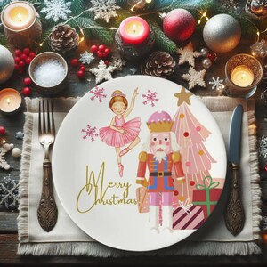 May include: A white ceramic plate with a festive Christmas design. The plate features a ballerina, a nutcracker, a pink Christmas tree, and the words "Merry Christmas" in gold script. The plate is set on a table with holiday decorations.