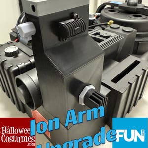 May include: A black and gray prop with the text "Ion Arm Upgrade". The prop has a boxy design with various attachments, including a cylindrical component and a white plug. The top section is gray.