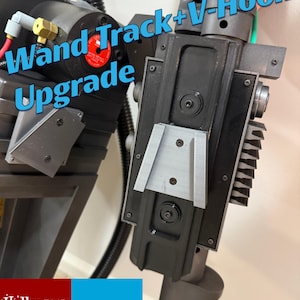 May include: Close-up of a black and gray Wand Track + V-Hook Upgrade. The upgrade features a silver V-shaped component and is attached to a larger, detailed device. The text "Wand Track + Upgrade" is visible in the image.