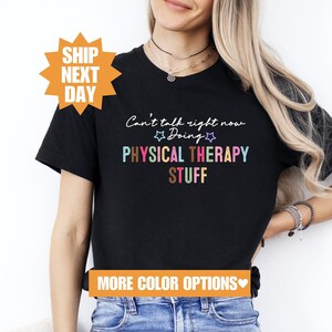May include: Black t-shirt with the text "Can't talk right now Doing PHYSICAL THERAPY STUFF" in rainbow colors. The text is written in a casual, handwritten style.