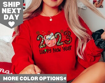 May include: Red sweatshirt with a graphic of a snowman in a mug with the text "2023 Happy New Year".