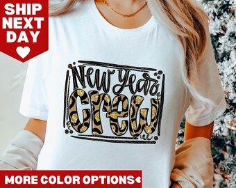May include: White t-shirt with the text "New Year's Crew" in black lettering with a leopard print design.