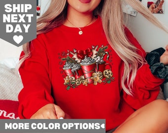 May include: Red Christmas sweatshirt with a graphic of three mugs of hot chocolate with whipped cream, gingerbread cookies, and candy canes.
