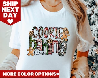 May include: White t-shirt with a Christmas-themed design that says "Cookie Baking Crew". The design features gingerbread men, plaid patterns, and cookies.