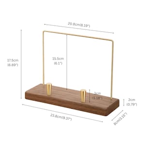 May include: A wooden jewelry display stand with a rectangular base and a gold-colored metal frame. The base is 9.37 inches long, 3.15 inches wide, and 1.18 inches thick. The frame is 8.19 inches wide and 6.1 inches tall.