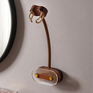 Pu&ograve; includere: Un supporto da parete in legno per asciugacapelli con un braccio curvo e una base in acrilico trasparente e scanalato. Il supporto presenta dettagli metallici color oro ed &egrave; realizzato in legno marrone scuro. Il design &egrave; moderno e minimalista.