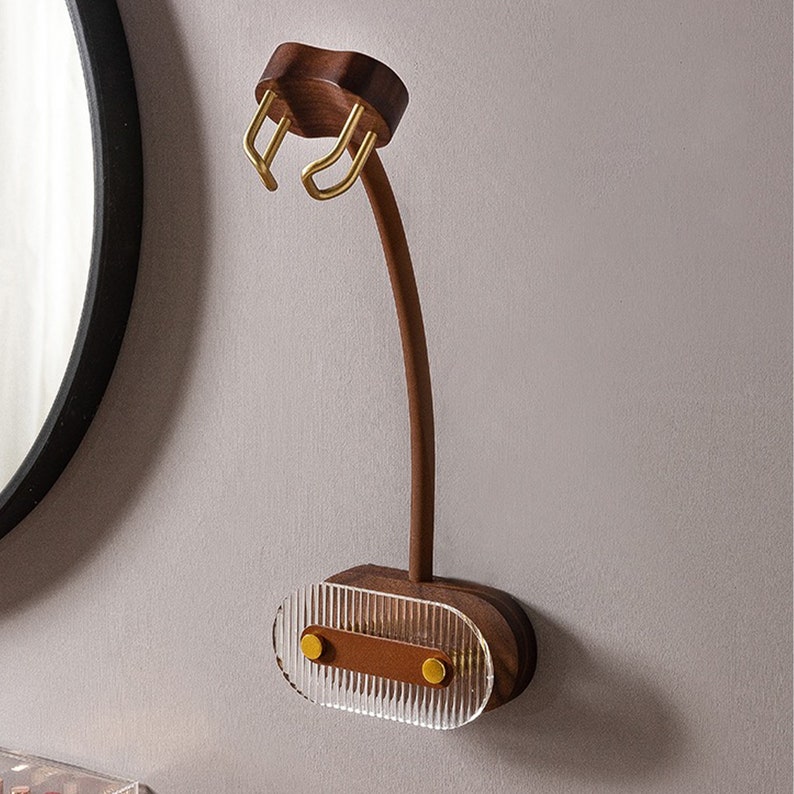 Pu&ograve; includere: Un supporto da parete in legno per asciugacapelli con un braccio curvo e una base in acrilico trasparente e scanalato. Il supporto presenta dettagli metallici color oro ed &egrave; realizzato in legno marrone scuro. Il design &egrave; moderno e minimalista.