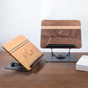 May include: Two wooden book stands with black metal bases. One stand is light wood with the name "A. Jackson" engraved. The other is dark wood with the name "David William" engraved. Both stands have a metal page holder.