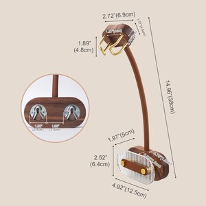 Pu&ograve; includere: Un espositore per gioielli in legno con un braccio marrone curvo e una base con una superficie trasparente e scanalata. Il supporto &egrave; alto 38 cm e presenta dettagli color oro. La parte superiore ha due ganci per appendere gioielli.