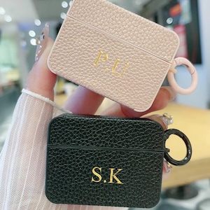 May include: Two personalised leather Airpod cases. One is pink with the initials "P.U." and the other is black with the initials "S.K."