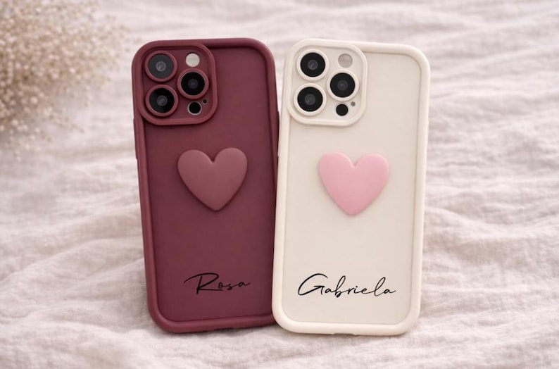 Może przedstawiać: Dwa etui na telefon: jedno bordowe, drugie kremowe. Każde ma serce i imię w skrypcie. Bordowe etui ma napis "Rosa", kremowe "Gabriela". Oba etui mają wycięcia na aparat.