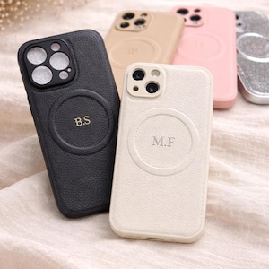 May include: A collection of personalized phone cases in various colors, including black, beige, pink, and silver. The cases feature a circular design with initials, such as "B.S" and "M.F."