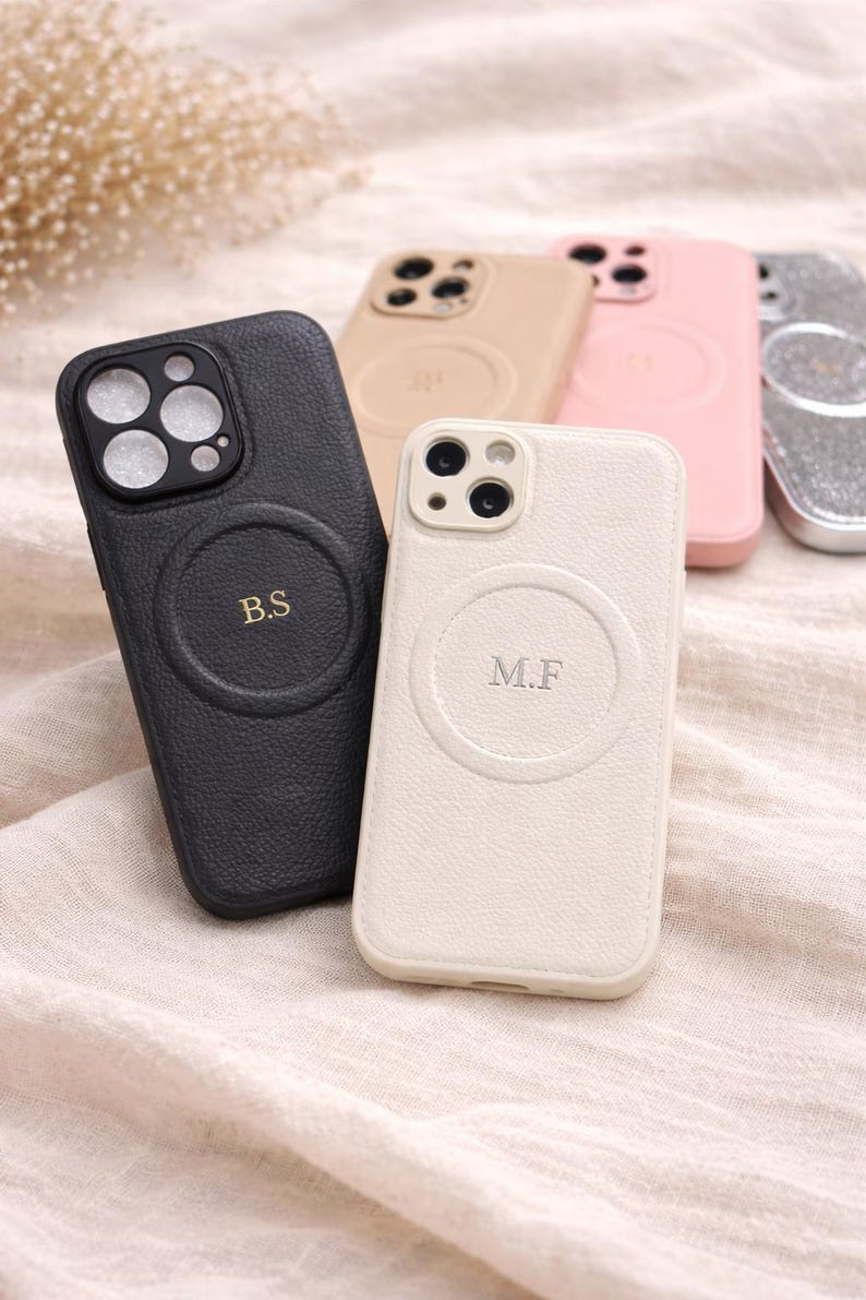 May include: A collection of personalized phone cases in various colors, including black, beige, pink, and silver. The cases feature a circular design with initials, such as "B.S" and "M.F."