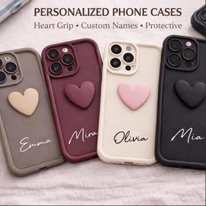 May include: Four personalised phone cases in taupe, burgundy, cream, and black. Each case has a 3D heart and a custom name in script. The cases are designed for phone protection.