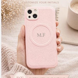 May include: A light pink personalized leather phone case with the initials "M.F" in a circular design. The case has a textured surface and the text "PERSONALIZED LEATHER PHONE CASE" is visible. The case is designed to be customized.