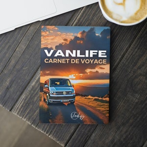 May include: A blue van with a sunset in the background. The van is on a dirt road and the text "VANLIFE CARNET DE VOYAGE" is on the cover of the book. The book is on a wooden table with a laptop and a cup of coffee.