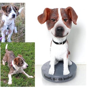 May include: A bobblehead figurine of a brown and white dog with a black collar. The dog is sitting on a gray base with the text "Russell, the 4th brother!" written on it.