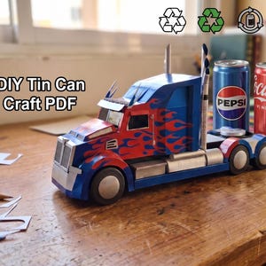 May include: A DIY craft project featuring a paper truck model with blue and red flame designs, parked next to Pepsi and Coca-Cola cans. The text "DIY Tin Can Craft PDF" is visible.