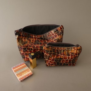 May include: Two zippered pouches featuring a brown and black crocodile skin pattern, a gold-toned rectangular lipstick case, and a small rectangular compact mirror with a multi-colored geometric pattern in shades of orange, blue, and white.