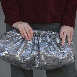 Può includere: Una pochette in pelle di serpente argentata e marrone con un design plissettato.