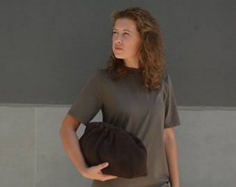Puede incluir: Una mujer con una camiseta marrón sostiene un bolso de mano de tela marrón.