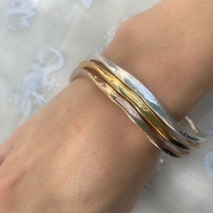 Può includere: Tre braccialetti d'argento impilati con una texture martellata. Il braccialetto superiore è d'oro, quello intermedio è oro rosa e quello inferiore è d'argento.