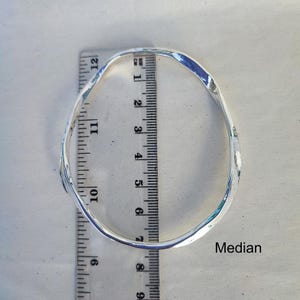 Puede incluir: Un brazalete plateado de estilo martillado. El brazalete tiene aproximadamente 7,6 cm de di&aacute;metro. Se coloca una regla junto al brazalete para medir. La palabra "Median" est&aacute; escrita en la superficie.