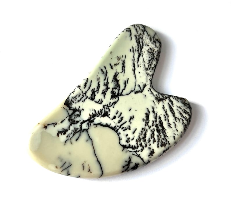 May include: A cream-colored, teardrop-shaped stone with a handle. The stone features intricate black veining patterns throughout, creating a unique, natural design. The smooth, polished surface reflects light, highlighting the contrasting colors and textures.