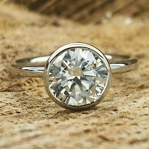 Può includere: Un anello d'argento con una montatura a castone che presenta un grande diamante rotondo e trasparente.