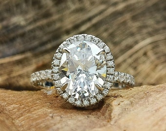 Könnte beinhalten: Ein silberner Verlobungsring mit einem großen ovalen Diamanten, der von einem Heiligenschein aus kleineren Diamanten umgeben ist.