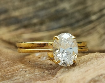 May include: A gold ring with a large oval-shaped diamond. The ring is set on a wooden surface.